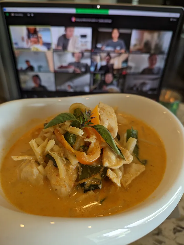 A bowl of Thai red curry with chicken and vegetables, with a Zoom call visible in the background.