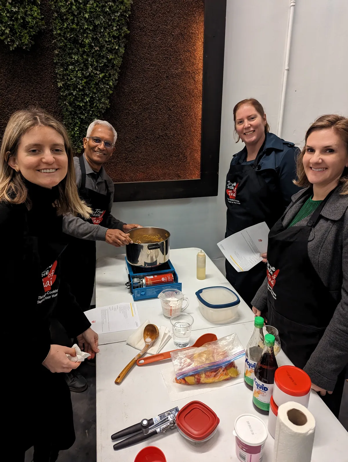 Four participants enjoy a Thai red curry cooking class in San Diego, gathering around a table filled with ingredients.