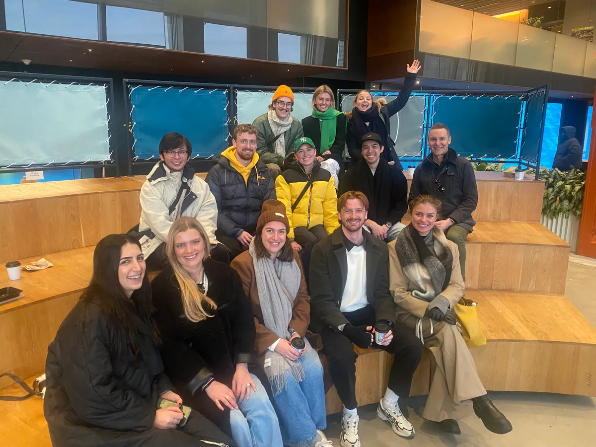 Group photo of a team at a VIP Seated Food Tour Experience in NYC, smiling and posing on wooden steps indoors.